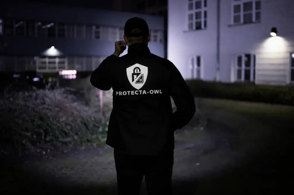 Sicherheitskraft mit Protecta-OWL-Jacke bei einem nächtlichen Kontrollgang im Außenbereich